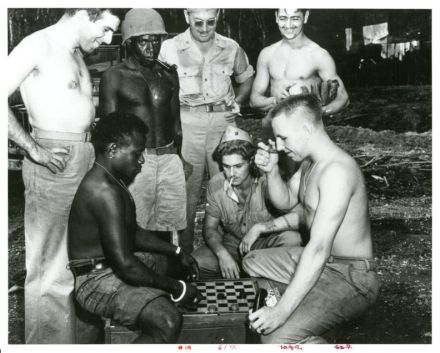 <p>Playing checkers, 1943<br />
Guadalcanal, Solomon Islands<br />
Photograph by Corporal A. M. Dileon</p>
<p>U.S. servicemen, who were stationed throughout the Pacific during World War II to reclaim and defend the islands, shared their pastimes with local residents during downtime. In this image, Private First Class William F. Fey (seated, right) is beaten at checkers by Guadalcanal resident Matthew Lova as other soldiers look on.</p>
<p>National Archives and Records Administration, Still Picture Unit, 127-GW-911-58947</p>
